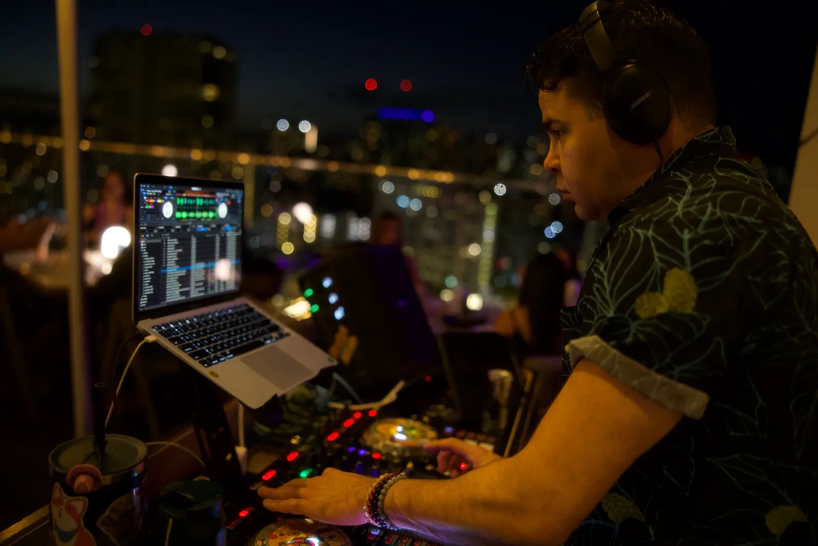 Billy Sage 5 mixing an open-format DJ set at dusk with the Honolulu skyline behind him